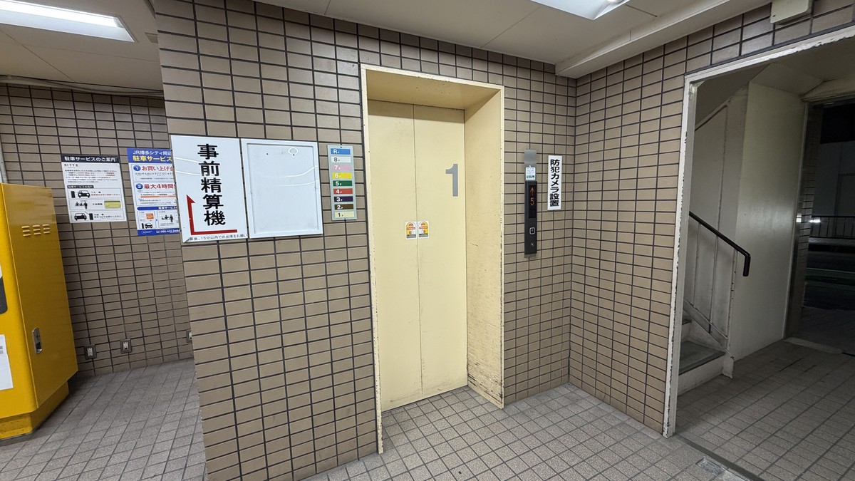 エレベーターホール。R階・8階〜1階まであり、防犯カメラを設置。事前精算機への案内表示もあります。